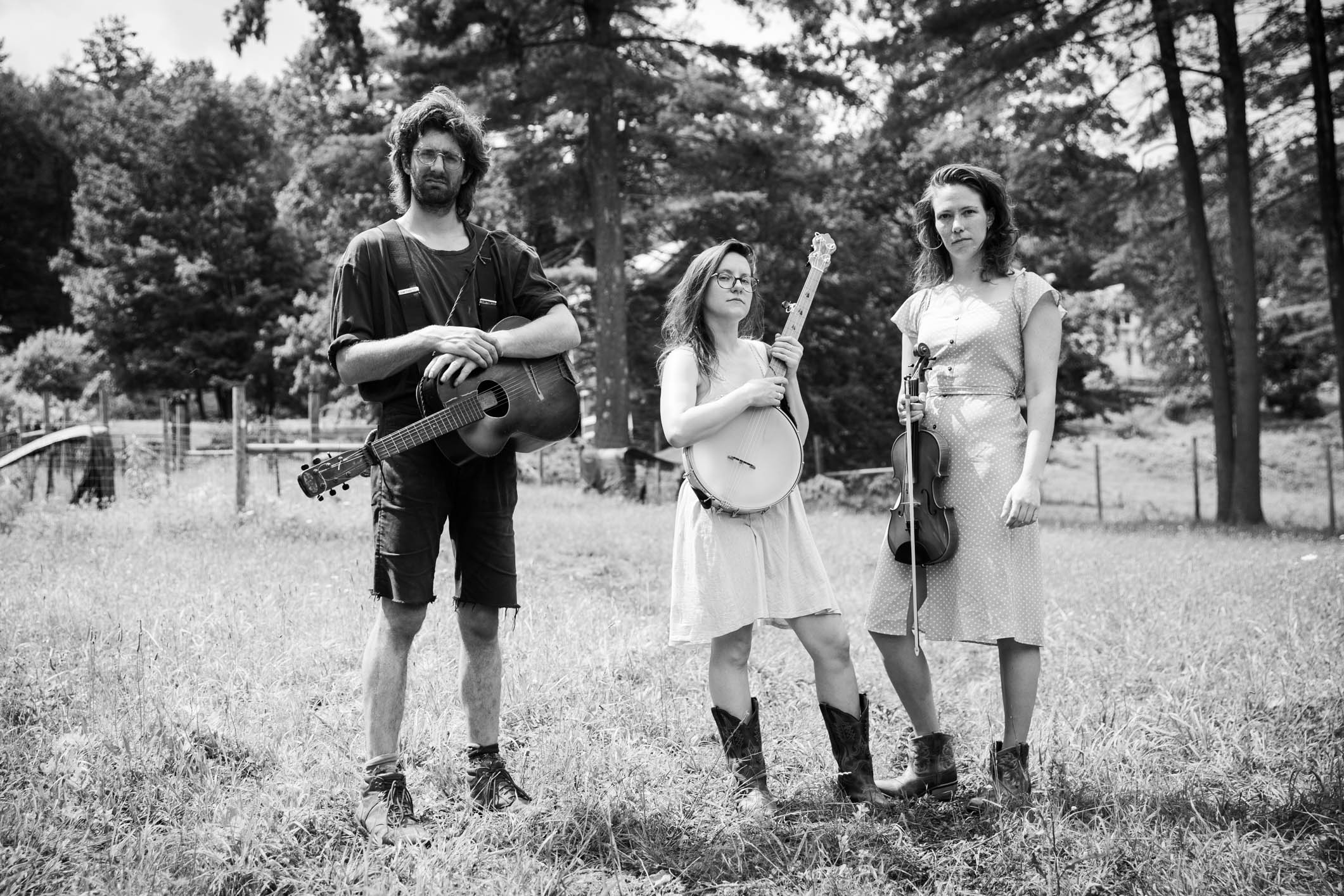 The three members of the band stand with their instruments in a field.